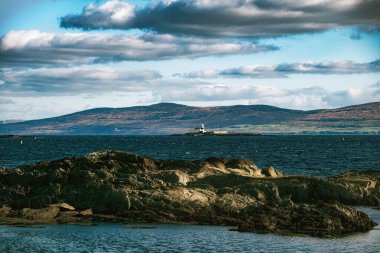 Kırmızı çatılı beyaz bir deniz feneri sakin, mavi suyla çevrilidir..