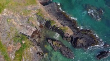 Su yavaşça kayalara çarpıyor, huzur ve sükunet hissi yaratıyor. Kayalar doğal bir heykele benzeyen bir şekilde dizilmiş gibi görünüyor..