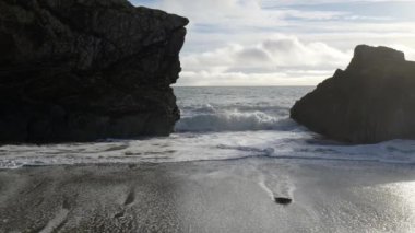 Dalgaların çekildiği kumlu bir sahil. Kıyı iki kayalık kayalık tarafından kuşatılmış ve dar bir geçit oluşturuyor. Dalgalardaki beyazlamalarla okyanus sakin..