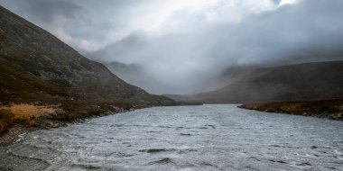 Sis çökerken ve etrafındaki tepeleri bir gizem ve dehşet perdesiyle örterken rüzgâr, girdaplı, dokulu bir yüzey oluşturuyor..