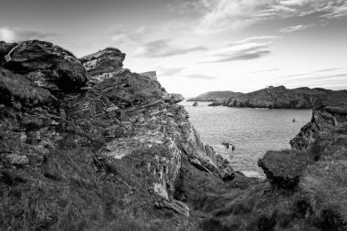 Sakin bir kıyı manzarası engebeli kayalıkları ve alacakaranlıkta sakin suları gösteriyor. Sahne, gölgelerin ve ışığın zıtlığını kayalara yansıtıyor ve sakin bir atmosfer yaratıyor..