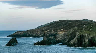 A view of a rocky coastline with a blue ocean. The water is a deep blue in color. The sky is clear and blue. The rocks are jagged and weathered. clipart