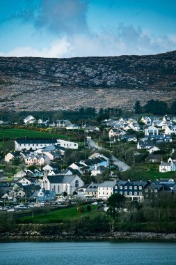 Aşağıda bir dizi beyaz evin bulunduğu eğimli, çimenli bir yamaç. Yamaçta yeşil çimenler ve ağaçlar var ve evler çalılıklarla çevrili..