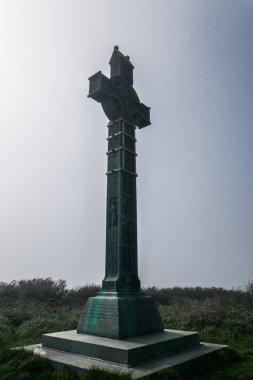 İrlanda 'da sisli tarlaların arasında uzun bir Kelt haçı duruyor, sakin bir sabah boyunca yerel tarih ve ruhaniliğin anısına..