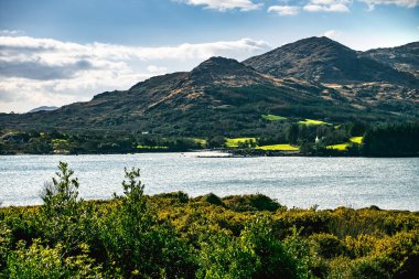 Önünde bir vadi ve bir su kütlesi olan bir dağ sırası..