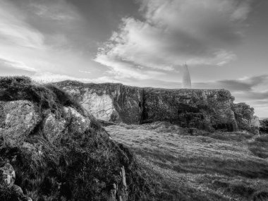 Yüksek açılı bir kıyı manzarası. İnce, beyaz bir kule, koyu renkli kayaların üzerinde duruyor. Gökyüzü görünür..