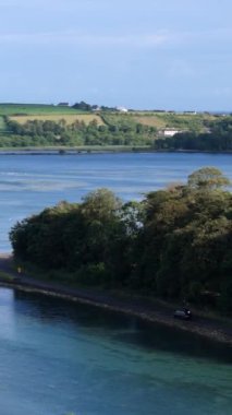 Ağaçların arasından güzel bir nehir akıyor, arka planda tepeler var. Güneş parlıyor, sakin bir atmosfer yaratıyor. Rahatlamak ve doğanın tadını çıkarmak için mükemmel..