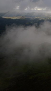 Bulutlar alacakaranlıkta engebeli dağların üzerinde yavaşça süzülürken nefes kesici bir manzara beliriyor. Uzak vadiler ve tepeler akşam gökyüzünün altında sakin bir zemin oluşturur..