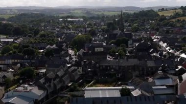 Ağırlıklı olarak gri çatıları olan yeşil alanlar ve önemli bir kilise kulesi olan bir kasabanın havadan görünüşü..