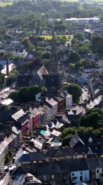 Gri çatıları ve yeşillikleri olan yoğun evler arasında belirgin bir çan kulesi olan bir kasaba, bir kilise oluşturur..