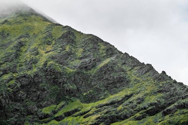 Carrauntoohil geçidi, İrlanda 'nın en yüksek zirvesinin manzaralı manzaralarının tadını çıkarıyor, yemyeşil ve bulutlu gökyüzünün altındaki engebeli araziyle çevrili..