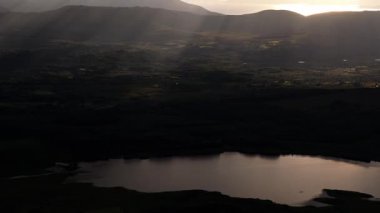 Sayısız tepe ve vadiler katmanlı bir manzara yaratır. Bulutlu bir gökyüzü güneş ışığının yere ulaşmasını sağlar..