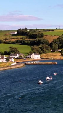 Sakin bir sahil topluluğu. Evler, çok sayıda küçük teknenin demirlediği suya yakındır. Nazik, yeşil tepeler sahneyi tamamlıyor..