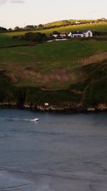 Altın saat boyunca, güzel bir sahil köyünün yakınındaki sakin sularda bir tekne süzülüyor. Yemyeşil tepeler ve büyüleyici evler manzarayı süslüyor. Huzurlu bir ortam..