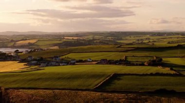 Gün batımında İrlanda kırsalının nefes kesici güzelliğini tecrübe edin. Yuvarlanan yeşil tepeler, yama alanları ve uzak çiftlikler sakin bir atmosfer yaratıyor..