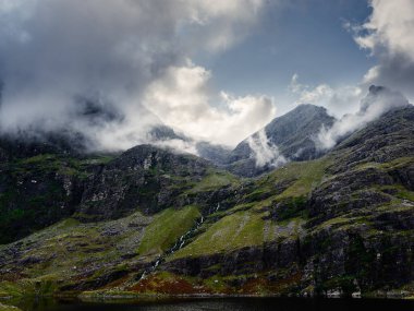 Engebeli dağlar ve alçak asılı bulutlarla çerçevelenmiş nefes kesici manzara Lough Gouragh. Huzur ortamı İrlanda 'nın doğal güzelliğini yansıtıyor..