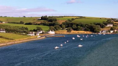 Birkaç küçük, beyaz ev sakin bir körfezin kıyısında yer alır. Birçok küçük tekne suda yüzer. Yuvarlanan yeşil tepeler köyün arkasında..