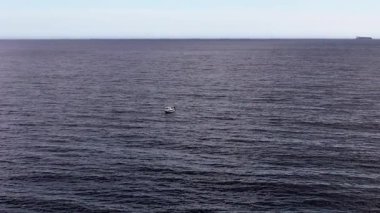 Küçük bir tekne, berrak bir gökyüzünün altında yumuşak dalgalarla çevrili engin denizde huzur içinde sürüklenir. Huzurlu manzara, sakinlik ve izolasyonun özünü yakalar..