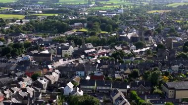 Videoda, gri çatılar ve önemli bir kilise kulesinin hakim olduğu bir kasabanın mimarisi sergileniyor. Yeşil alanlar her yerde görülür.