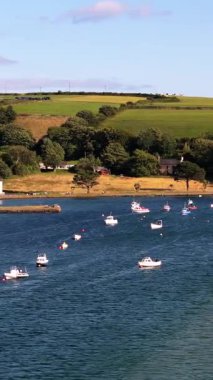 Resimli bir sahne. Evler körfez kıyısında, küçük tekneler demirli. Yeşil tepeler ve sakin su ile ortam huzurlu..