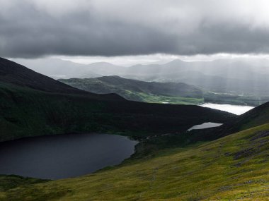 Bir vadiye yerleşmiş iki göl. Yuvarlanan yeşil tepeler fırtınalı bir gökyüzünün altında bir dağ sırasına yükselir..
