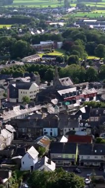 Gri çatılı evler ve bol yeşillik yüksek kilise kulesine sahip bir kasabanın havadan çekilmiş görüntüsünü oluşturur..