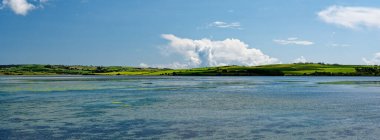 Durgun sular İrlanda 'daki Inchydoney Adası boyunca uzanır. Canlı yeşillikleri ve mavileriyle ziyaretçileri büyüler. Geniş gökyüzü, doğal güzelliği artıran tüylü beyaz bulutları barındırır..