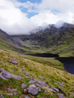 İrlanda 'nın Kerry ilçesinde gündüz vakti dağlarla ve bulutlarla çevrili Coomloughra Lough' un çarpıcı manzarası..