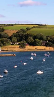 Evler ve küçük tekneler bir hangarı dolduruyor. Manzara sakin ve yeşil. Su koyu mavi. Güneşli bir gün.