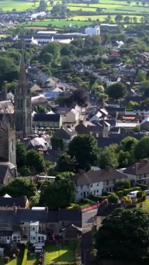 Video, gri çatıları, yeşil alanları ve kilise kulesi olan birçok evi gösteren bir kasabanın hava görüntüsü..