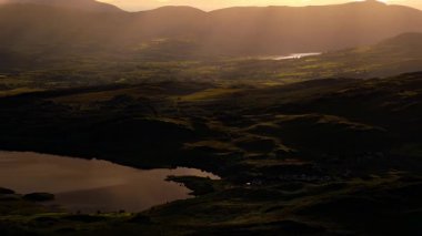 Göl manzaralı bir vadi. Arka planda dağlar. Güneş ışığı atmosferden süzülür.