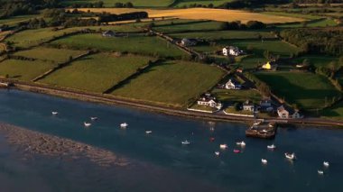 Canlı yeşil tarlaları ve dingin sularıyla nefes kesici İrlanda kırsalını keşfedin. Güneş batarken tekneler körfezde hafifçe sallanarak manzarayı güzelleştiriyor..