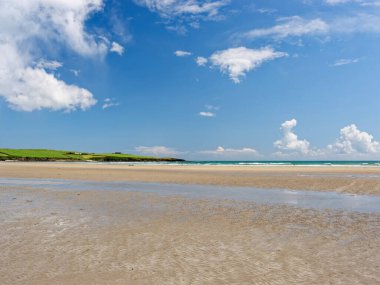 Huzurlu sahil manzarası. Geniş kumlu plaj, hafif dalgalar ve tüylü beyaz bulutlarla kaplı parlak mavi bir gökyüzü plajda huzurlu, huzurlu bir yaz günü yaratıyor..