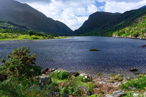 İrlanda 'da yemyeşil bir göl, engebeli tepeler ve yukarıda dinamik bulutlar vardır. Sakin sular yavaşça dalgalanır, sizi bu manzaralı alanı keşfetmeye davet eder..