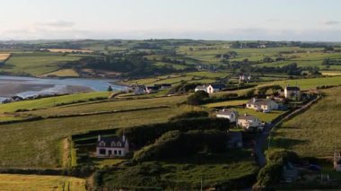 Altın güneş ışığı, İrlanda 'nın kırsal kesimindeki yemyeşil tepeleri ve antika evleri yıkıyor. Huzurlu kıyı şeridi, doğanın güzelliğini gözler önüne seren kırsal manzaraya cazibe katıyor..
