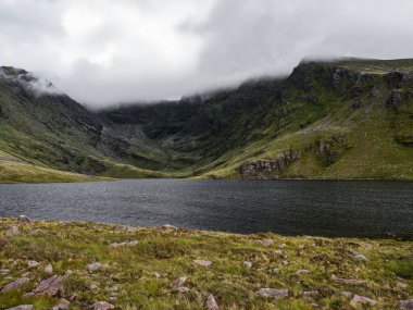 Coomloughra Lough 'un sakin suları İrlanda' da bulutlu bir gökyüzünün altındaki yeşil dağları yansıtır. Bu huzurlu yer doğayla barışçıl karşılaşmaları davet ediyor..