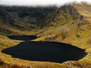 Coomloughra Lough, engebeli tepeler ve sisle çevrili sakin güzelliğini sergiliyor. Karanlık sular, doğa aşıkları için mükemmel bir ortam yaratıyor..