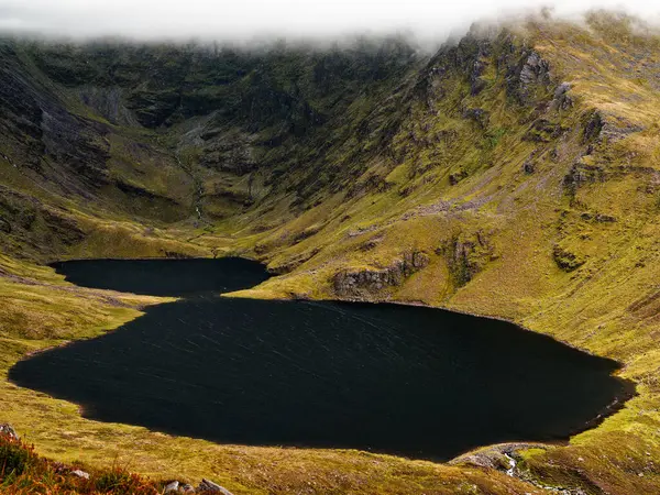 Coomloughra Lough, engebeli tepeler ve sisle çevrili sakin güzelliğini sergiliyor. Karanlık sular, doğa aşıkları için mükemmel bir ortam yaratıyor..
