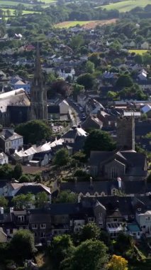 Video bir kasabanın mimarisini gösteriyor, esasen koyu gri çatıları olan küçük evler ve büyük bir kilise kulesi..