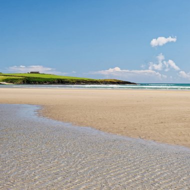 Kıyı sükuneti. Güneşli bir günde sakin bir kumsalın nefes kesici manzarası, canlı mavi bir gökyüzü ve yumuşak dalgalar, rahatlamak için mükemmel..