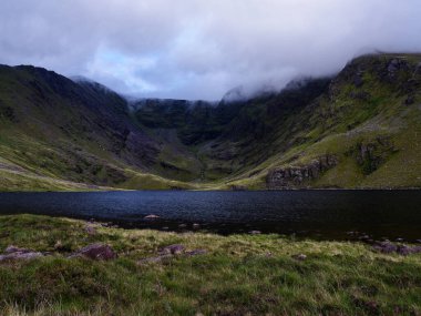 Dik yeşil vadilerde yuva yapmış Coomloughra Lough bulutlu gökyüzünü yansıtan sakin suları sergiler. Dramatik manzara İrlanda 'nın doğal güzelliğini alacakaranlıkta sergiliyor.