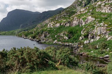 Ziyaretçiler, yemyeşil bitki örtüsünün bulutlu bir gökyüzünün altında engebeli kayalıklarla buluştuğu İrlanda 'daki Kara Göl' ün huzurlu atmosferinin tadını çıkarabilirler. Doğa bu resim ortamında gelişiyor..