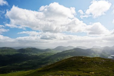 Yeşiller yemyeşil tepeler, İrlanda, BlackValley boyunca uzanır ve büyüleyici doğal güzellikleri gözler önüne serer. Büyüleyici bulutlar, parlak gökyüzünde tembelce sürükleniyor ve sakin bir atmosfer yaratıyor..