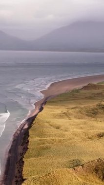 Huzurlu kıyı manzarası. Yuvarlanan kum tepecikleri kasvetli bir gökyüzünün altında düşen dalgalarla karşılaşır. Barışçıl bir kaçış.