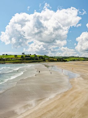West Cork, 25 Haziran 2023. Sahil sükuneti. Arkaplandaki yemyeşil tepelerle tezat oluşturan kumlu bir sahilde hafif dalgalar. Çok az insan sakin atmosferin tadını çıkarır..
