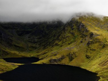 Coomloughra Lough, engebeli tepeler ve sisle çevrili sakin güzelliğini sergiliyor. Karanlık sular, doğa aşıkları için mükemmel bir ortam yaratır..