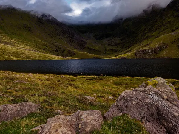 Coomloughra Lough, yemyeşil ve kayalık arazilerle çevrili İrlanda dağlarının kalbinde huzur içinde oturur. Üzerimizde kara bulutlar belirir..