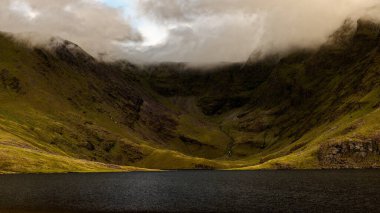 Coomloughra Lough, yemyeşil dağlar ve puslu bulutlarla çevrili sakin bir su kütlesi sergiliyor. İrlanda 'nın doğal güzelliğini gözler önüne seriyor..