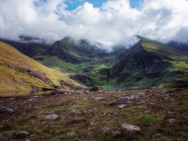 Lough Callee sakin sularını, yüksek dağlarını ve parçalı bulutlu bir gökyüzünün altında canlı yeşil manzaralarını sergiliyor. nefes kesici manzara..