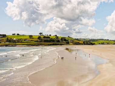 West Cork, 25 Haziran 2023. İnsanların yaz gününün tadını çıkardığı çarpıcı bir plaj manzarası. Kum, deniz ve yeşil tepeler arasındaki zıtlık huzurlu ve güzel bir manzara yaratır..